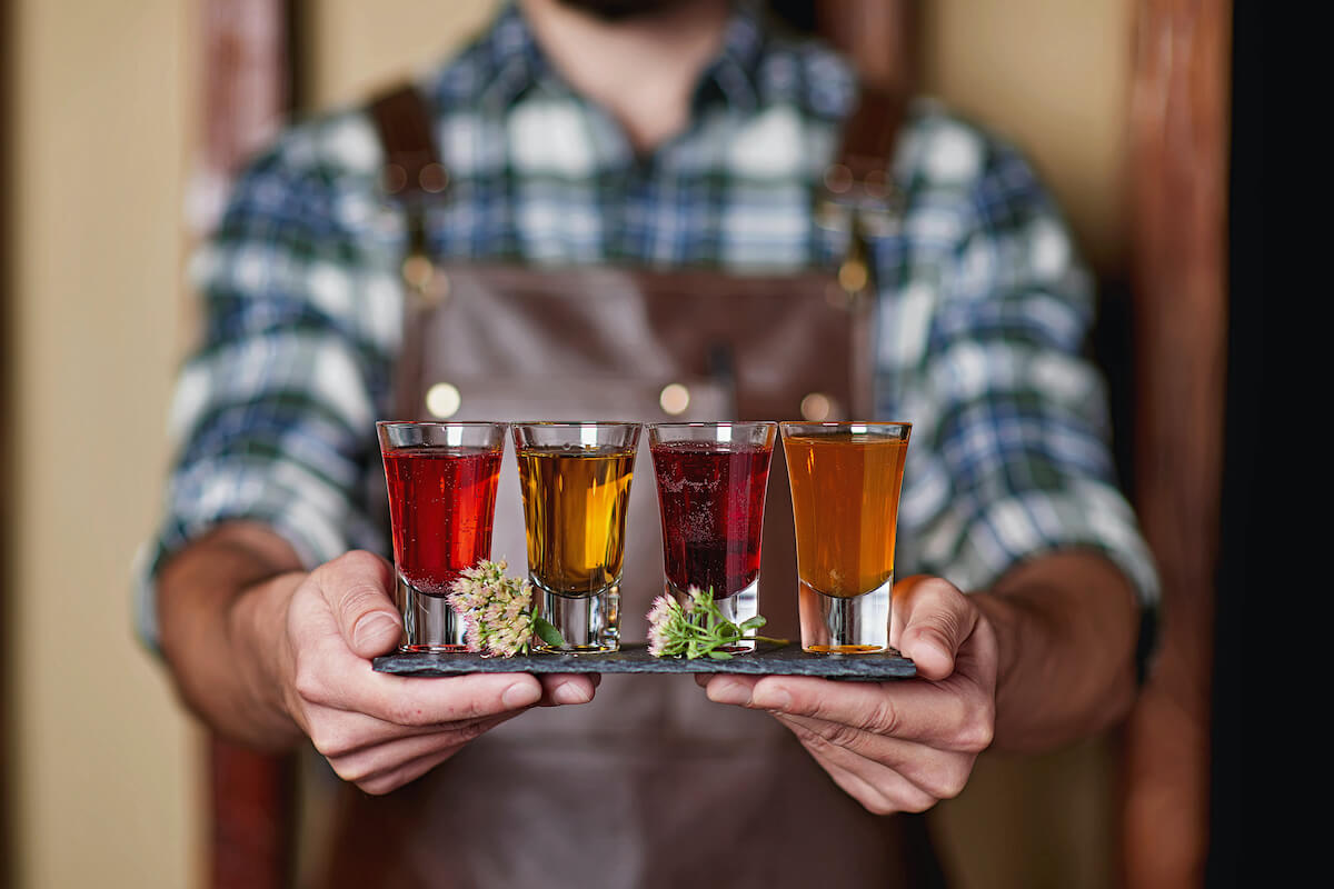 man in leather apron holding a flight of different colored moonshine